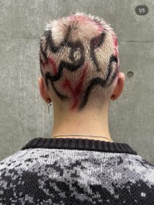 White-blonde buzz cut with hand-painted red and black tribal-inspired stripes.