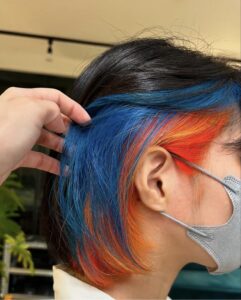 Close-up of inner color at Assort Osaka, featuring a high-contrast vivid blue and bright orange peek-a-boo section on dark hair.